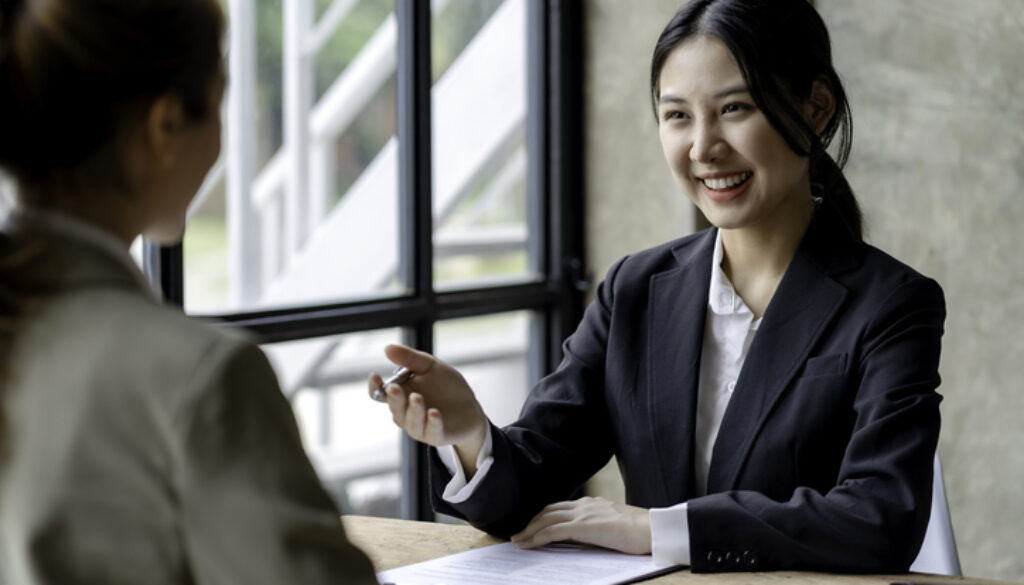 Smiling young Asian businesswomen talking to colleague and exchanging ideas together at office.