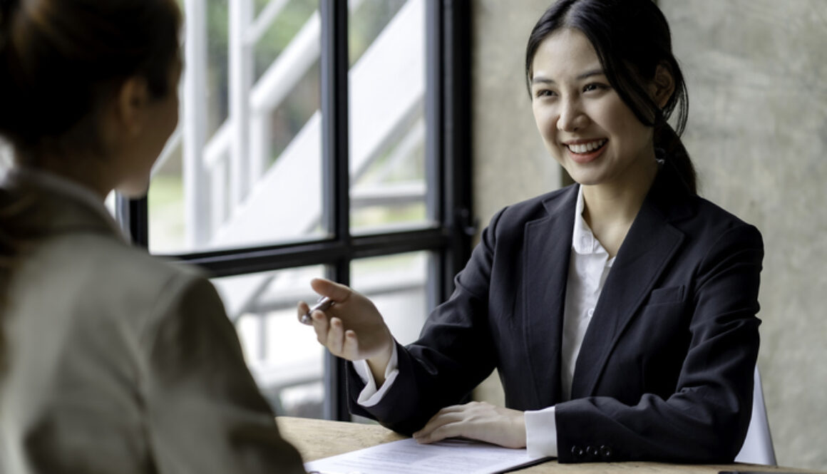 Smiling young Asian businesswomen talking to colleague and exchanging ideas together at office.